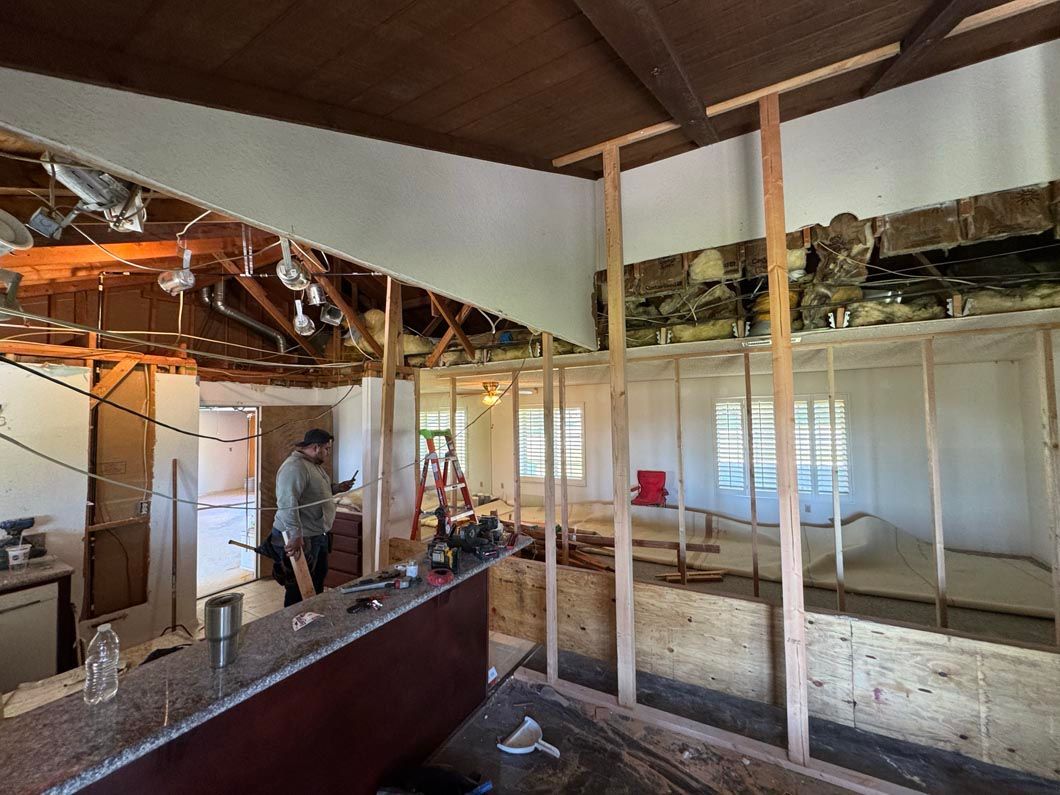 Partially renovated room with exposed ceiling beams, drywall, and a worker near the back wall