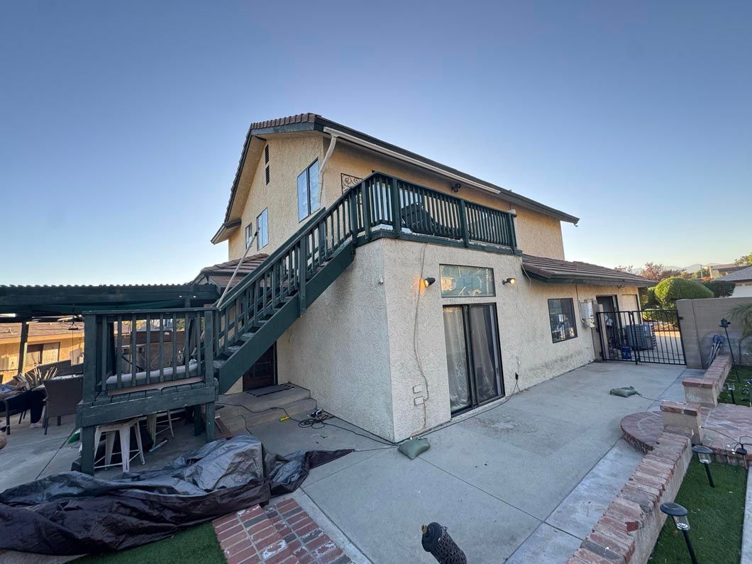 Two-story stucco house with exterior staircase and balcony in a courtyard at sunset