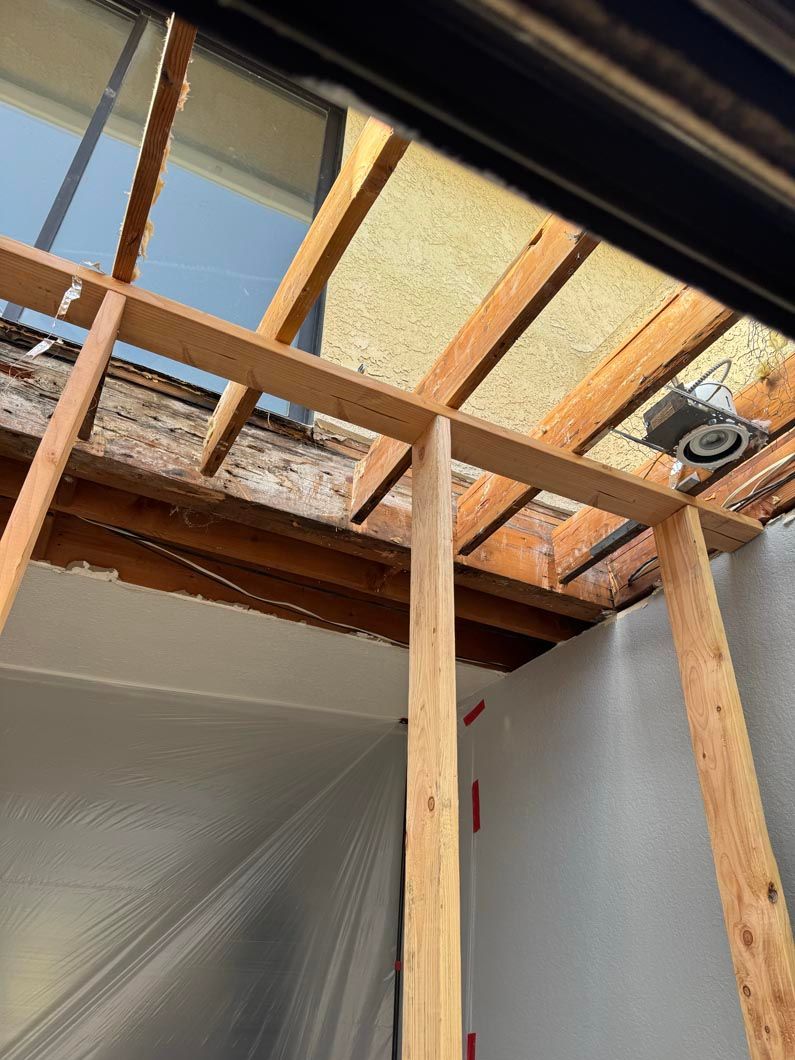 Exposed attic framing with wooden studs, insulation, and a skylight opening above a plastic-covered wall.