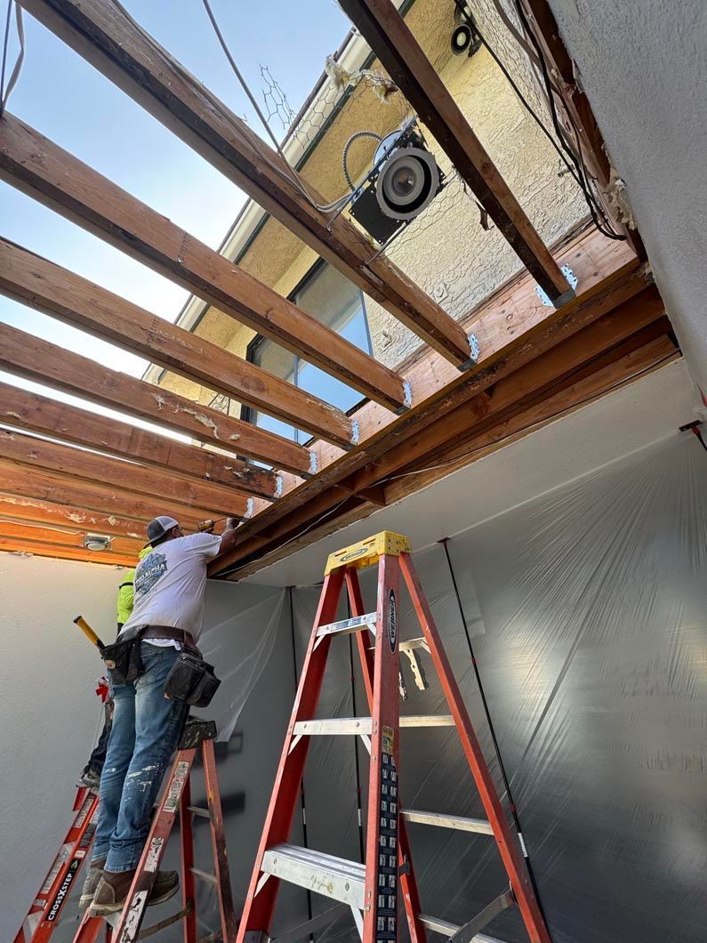 Worker on a ladder installing ceiling beams in a room under construction
