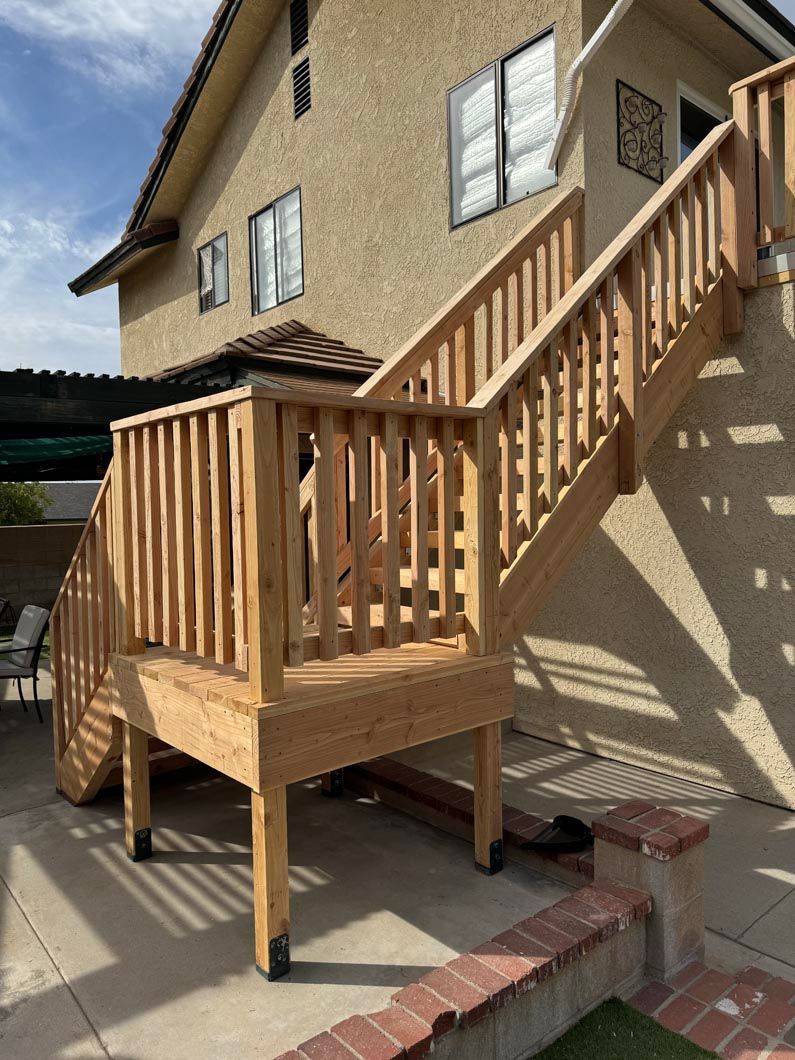 Wooden exterior staircase and small deck attached to a beige house on a sunny day