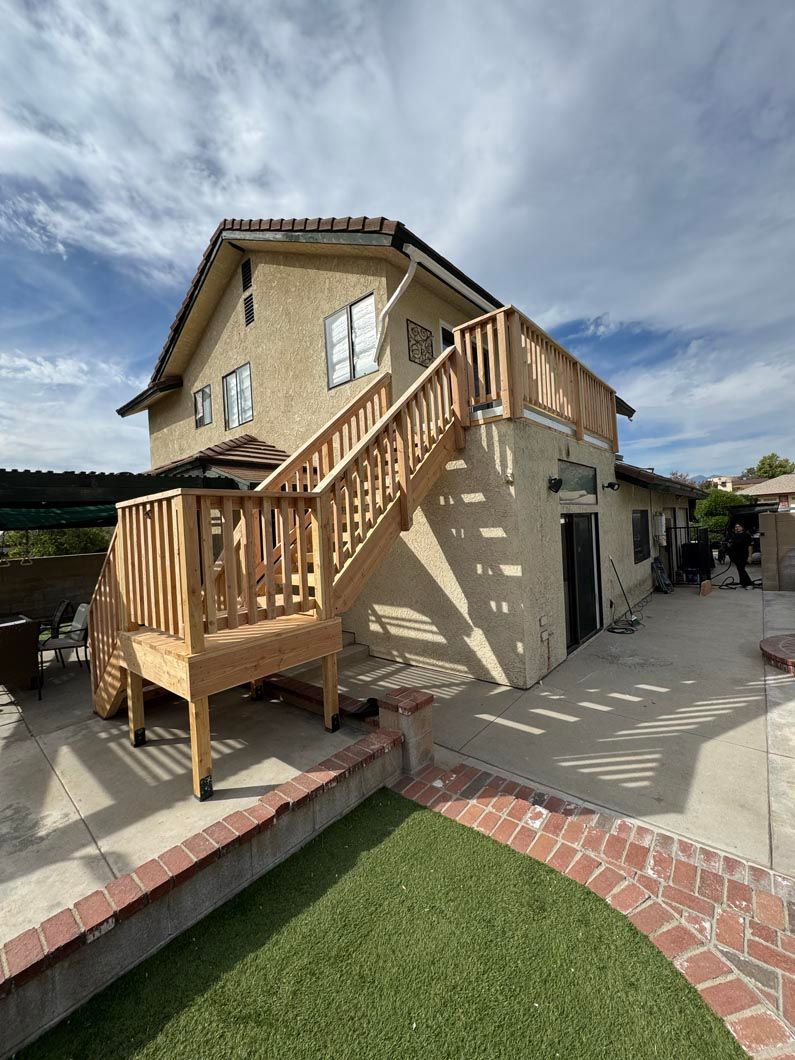 Two-story house with exterior wooden staircase and small front patio under a partly cloudy sky