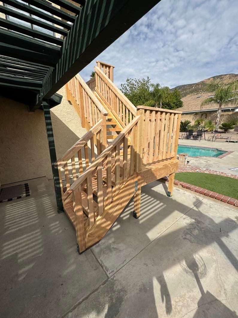 Wooden poolside staircase and deck beside a beige building, with mountains and a swimming pool in the background