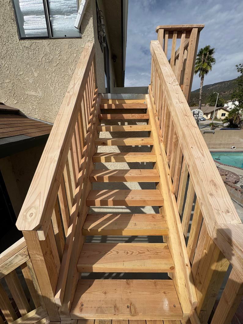 Wooden outdoor staircase with railings beside a house, leading up to a deck.