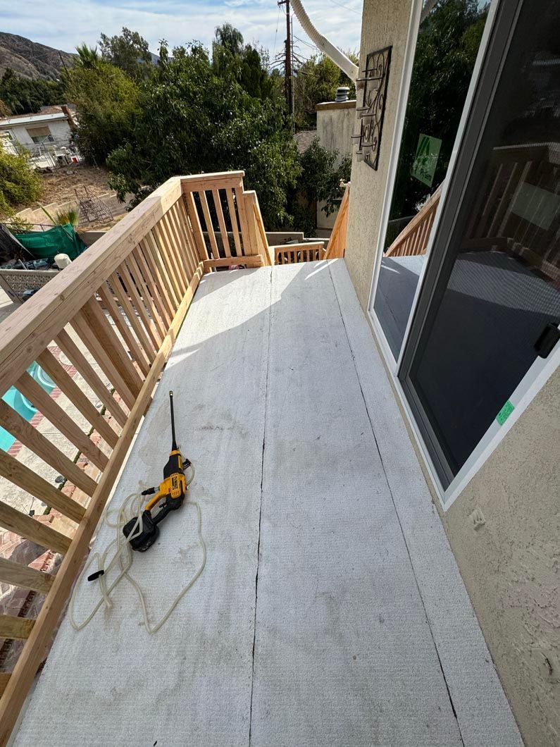 Wooden deck under construction with railing, scattered tools, and sliding glass door beside a hillside view