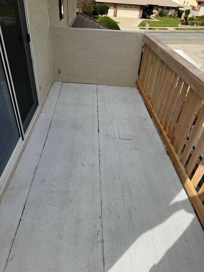 Narrow apartment balcony with concrete floor, beige walls, and a wooden railing in sunlight