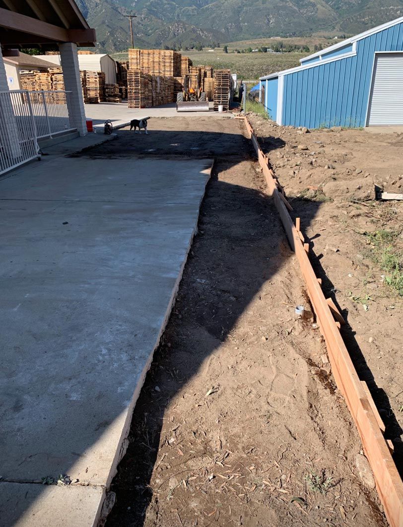 Construction site with a concrete slab, dirt path, orange pipe, and blue metal building