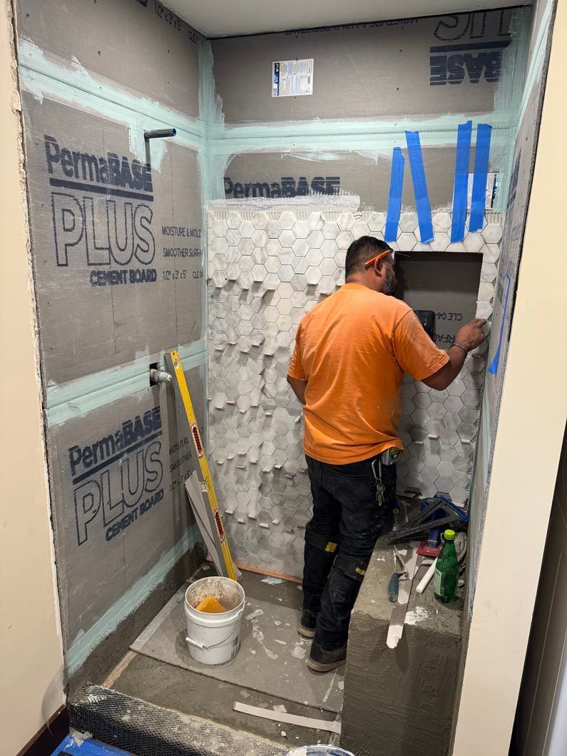 Worker in an orange shirt applies plaster to a bathroom wall during renovation.