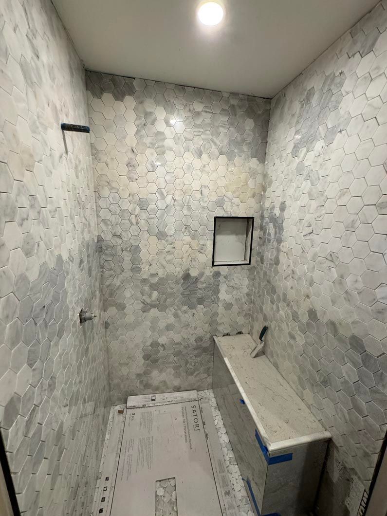 Small tiled bathroom under renovation with a shower area, toilet space, and a wall-mounted sink.