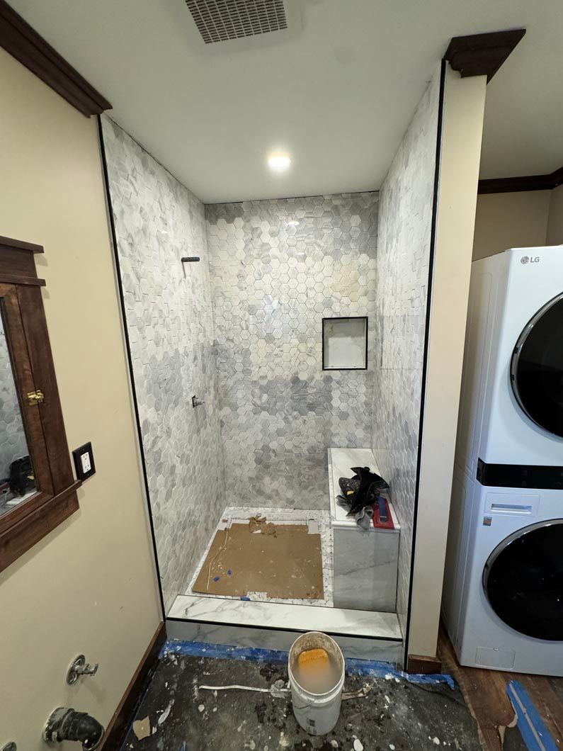 Small bathroom remodel with tiled shower, toilet, sink, mirror, and stacked washer and dryer.