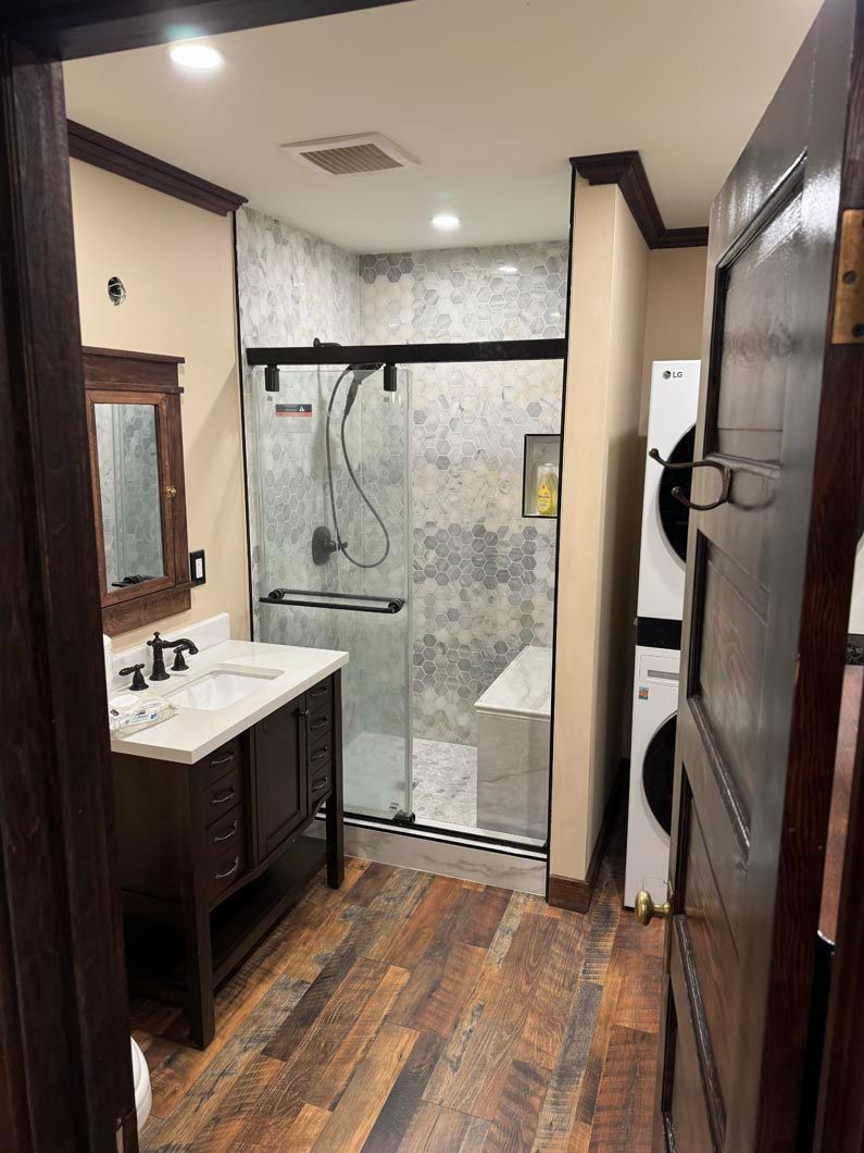 Bathroom with vanity, mirror, and walk-in shower with glass door and marble-pattern tile.