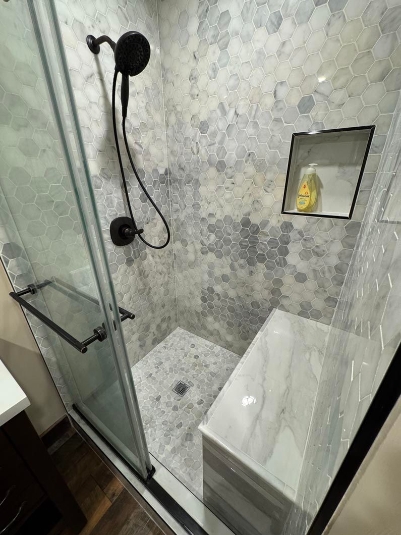 Small tiled shower with glass door, black fixtures, and a built-in shelf holding soap.