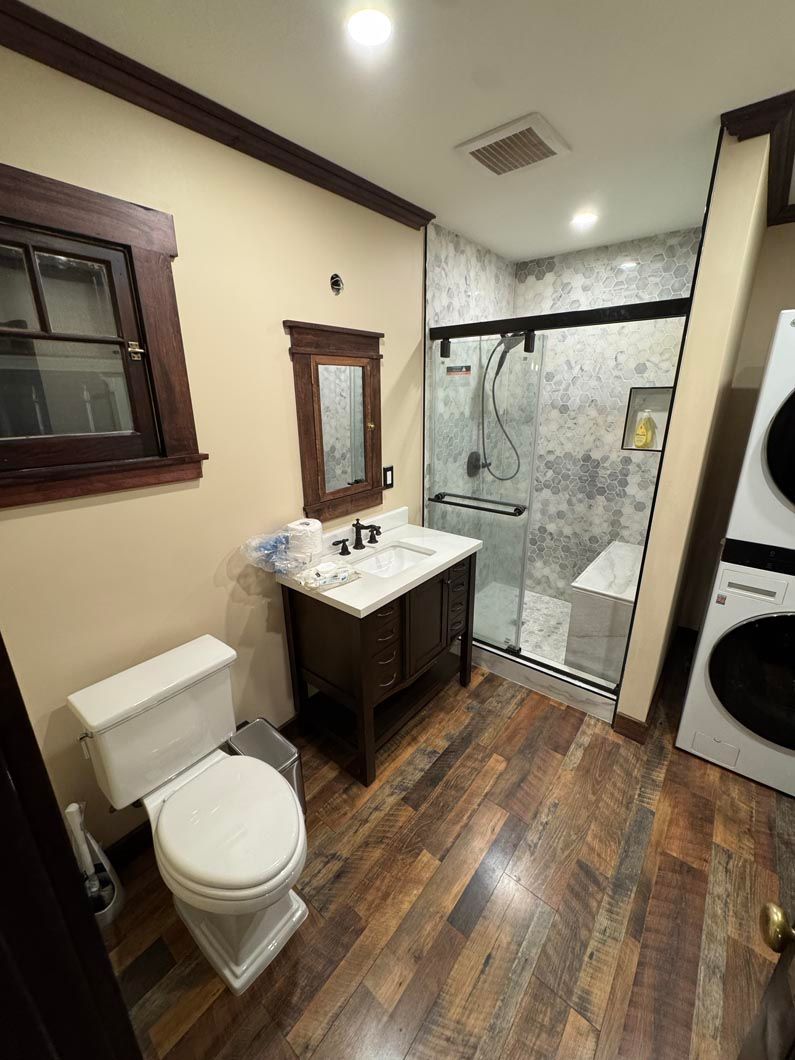 Small bathroom with toilet, vanity, mirror, wood floor, and glass walk-in shower.