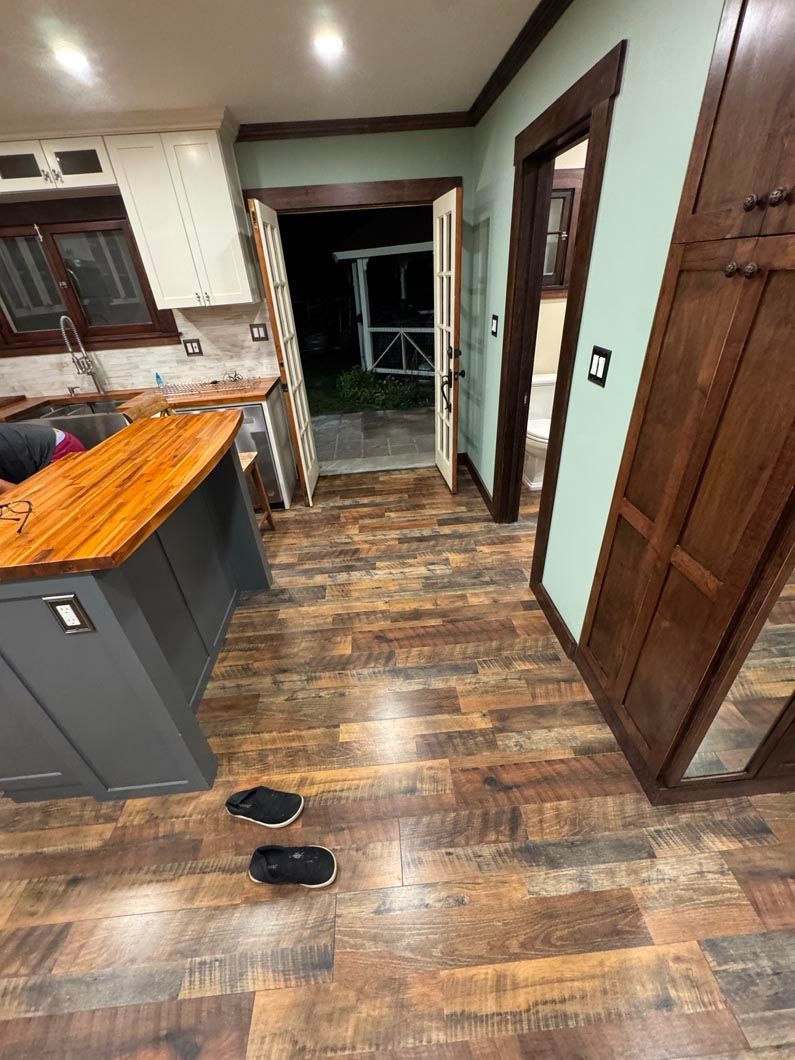 Kitchen with wood flooring, gray island, dark doorway, and two black slippers on the floor.