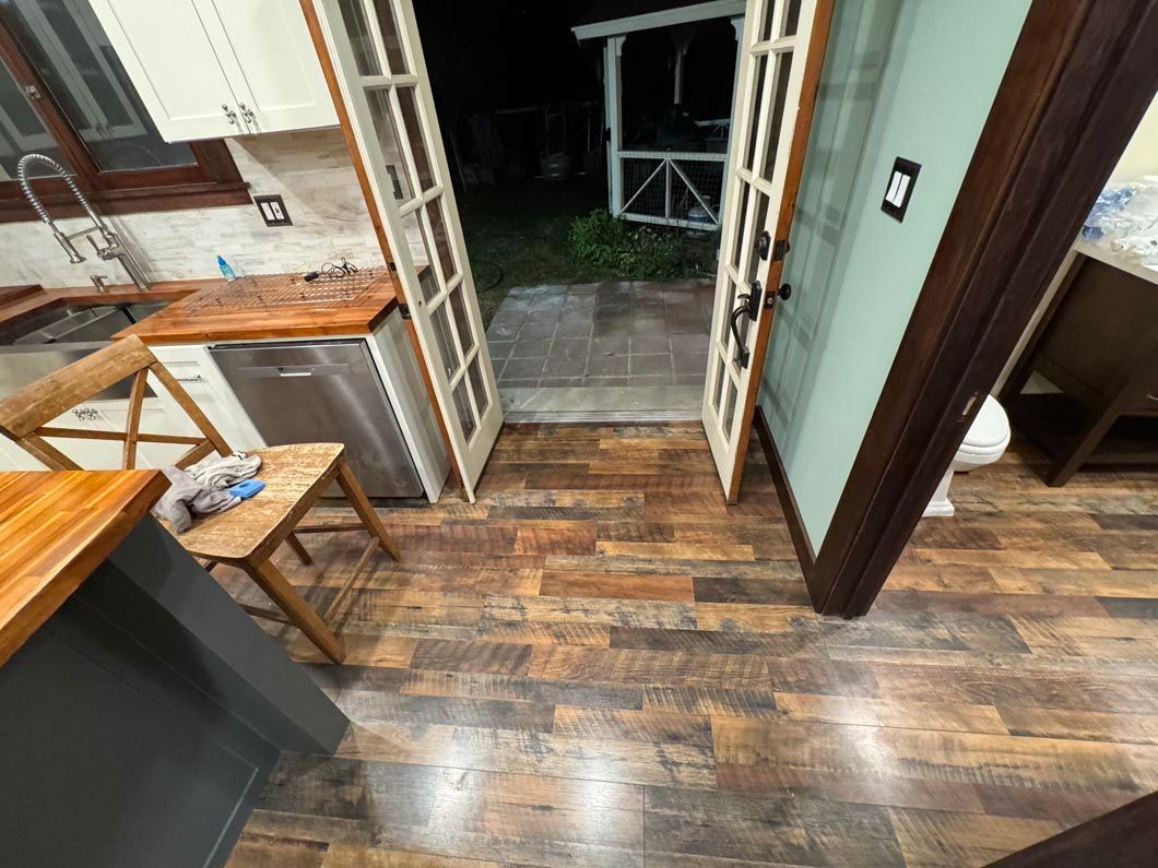 Indoor room with wood-look floor, open double doors, and a small table near a kitchen counter.