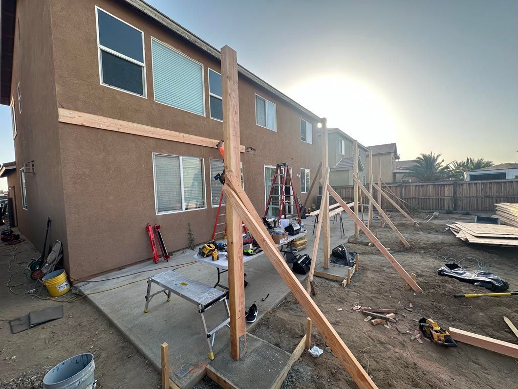 House under construction with wooden support braces and scattered building materials in a dusty yard