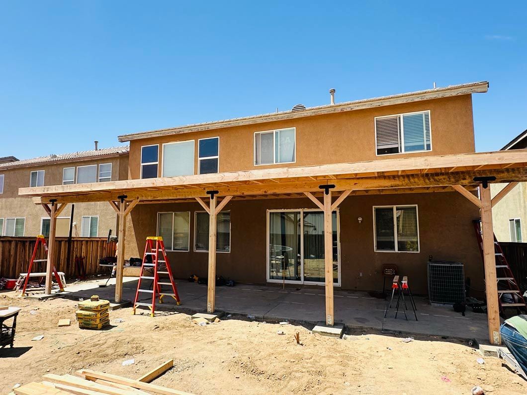 Two-story house under construction with stucco exterior, covered porch, and ladders in front