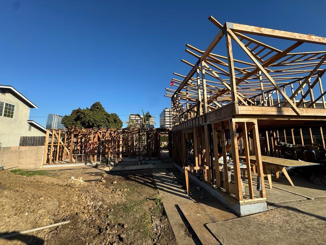Partially built wooden house frame on a sunny construction site with blue sky.