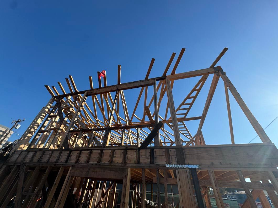 Wooden house frame under construction against a blue sky, with workers on the roof beams.