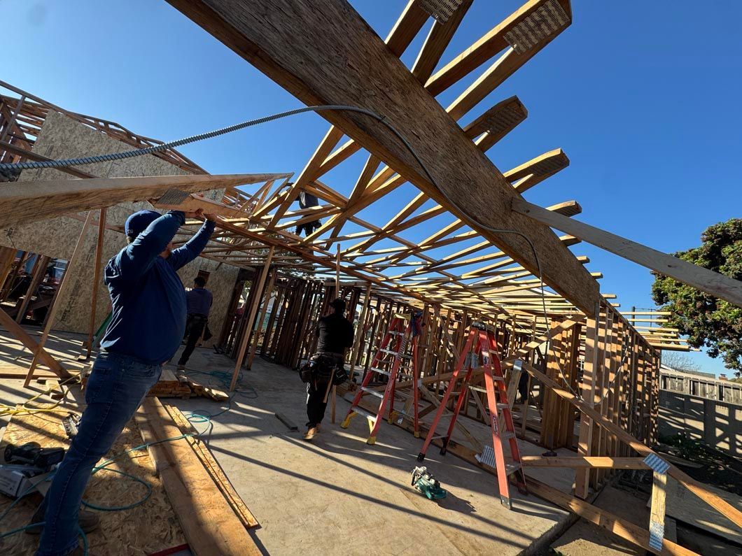 Workers building a wooden structure with red support poles under a bright blue sky