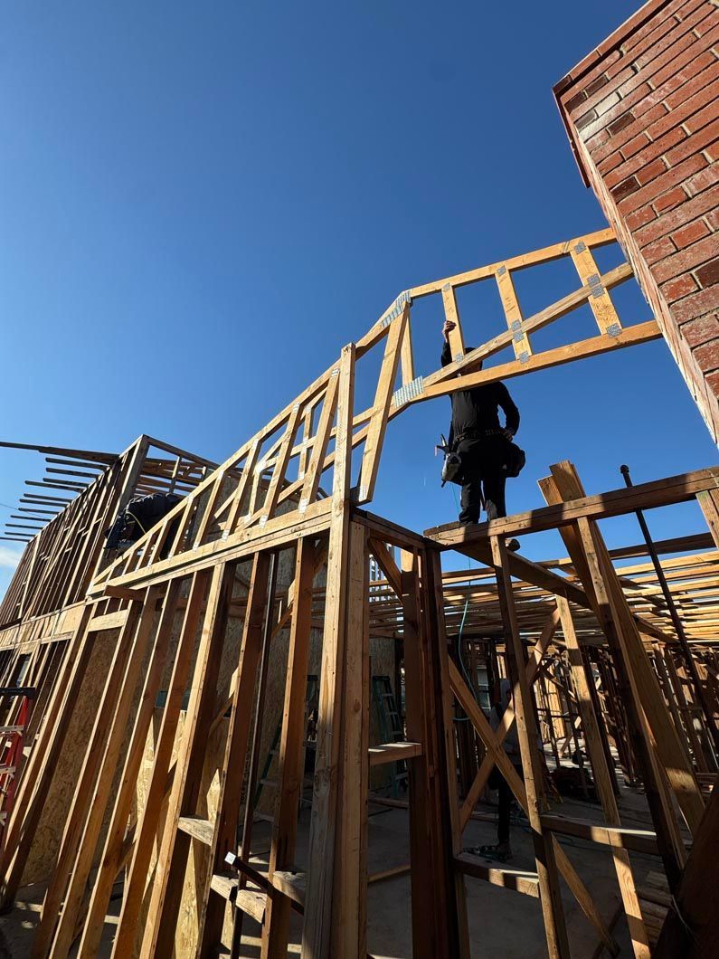 House framing under construction with a worker on the upper beams against a blue sky