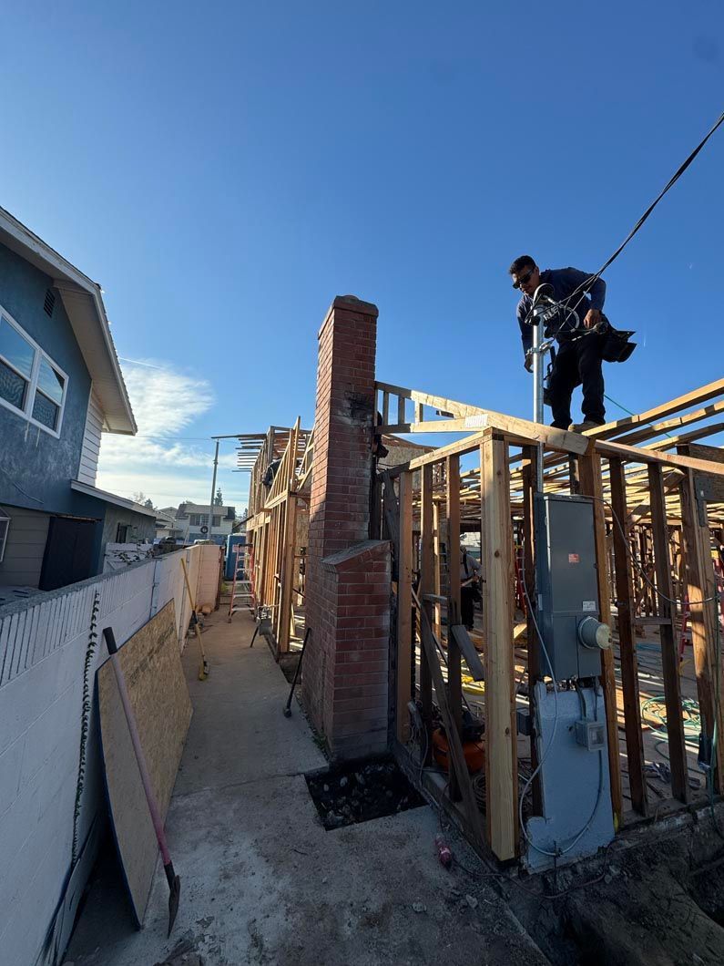 Worker on top of a wooden house frame during construction beside a brick chimney under a clear blue sky