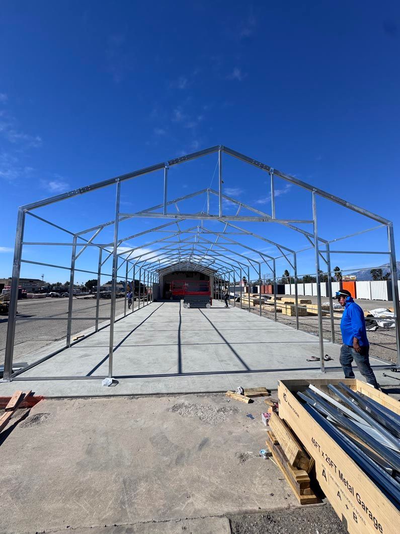 Steel frame structure under construction in an open lot, with a worker in a blue jacket at right.