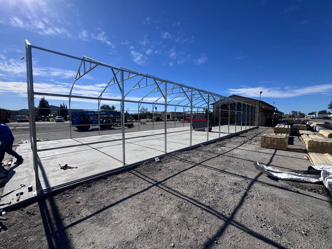 Construction site with chain-link fencing and a partially built steel frame under a blue sky.