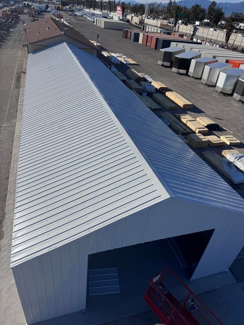 Aerial view of a long white metal warehouse roof in an industrial yard with containers and trucks nearby