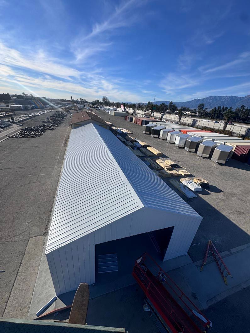 Aerial view of a large white warehouse building in an industrial yard with rows of containers and mountains beyond