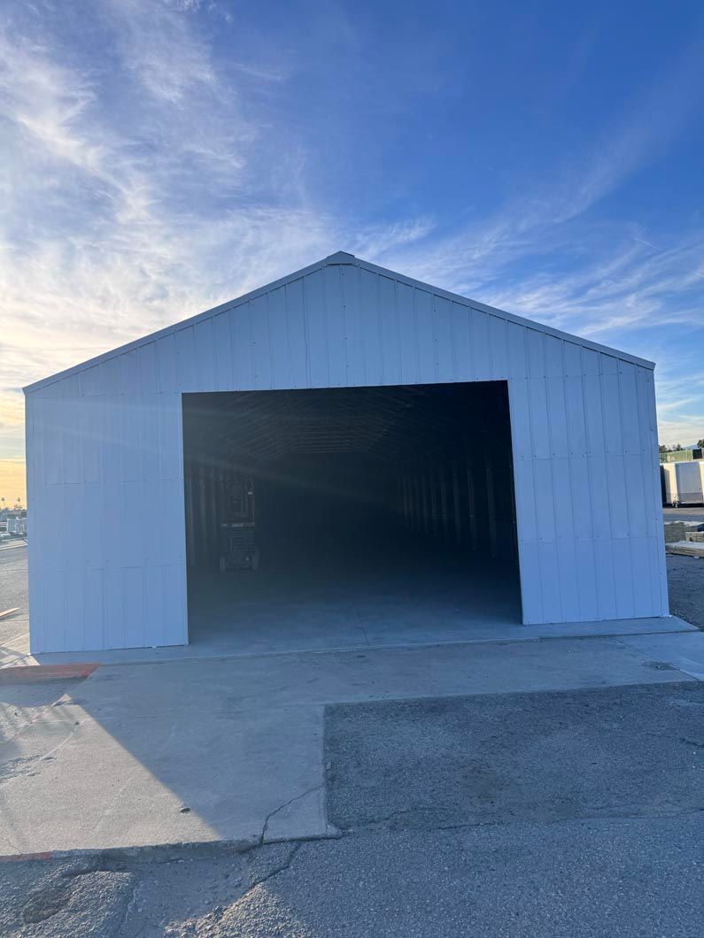 White metal warehouse with large open doorway on a concrete lot under a blue sky
