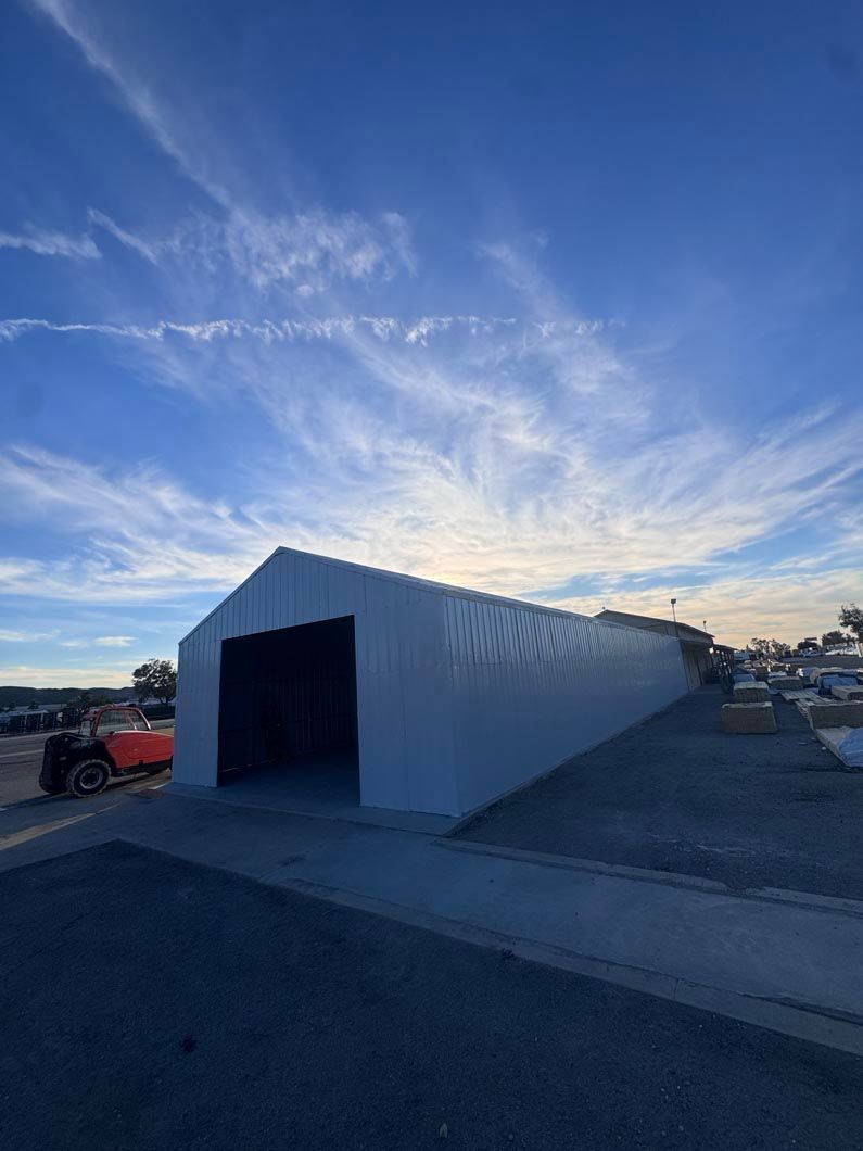 White metal storage tent at sunset with open entrance and a red vehicle parked beside it.