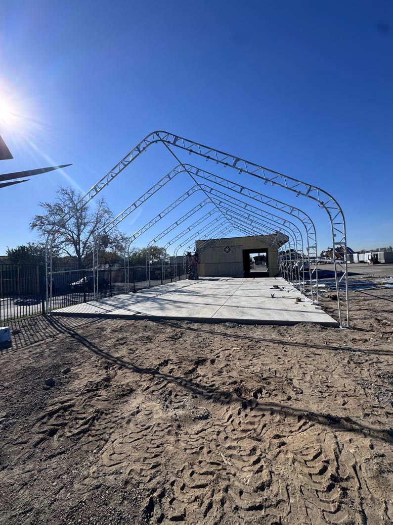 Outdoor construction site with steel arch frames over a concrete slab under a clear blue sky