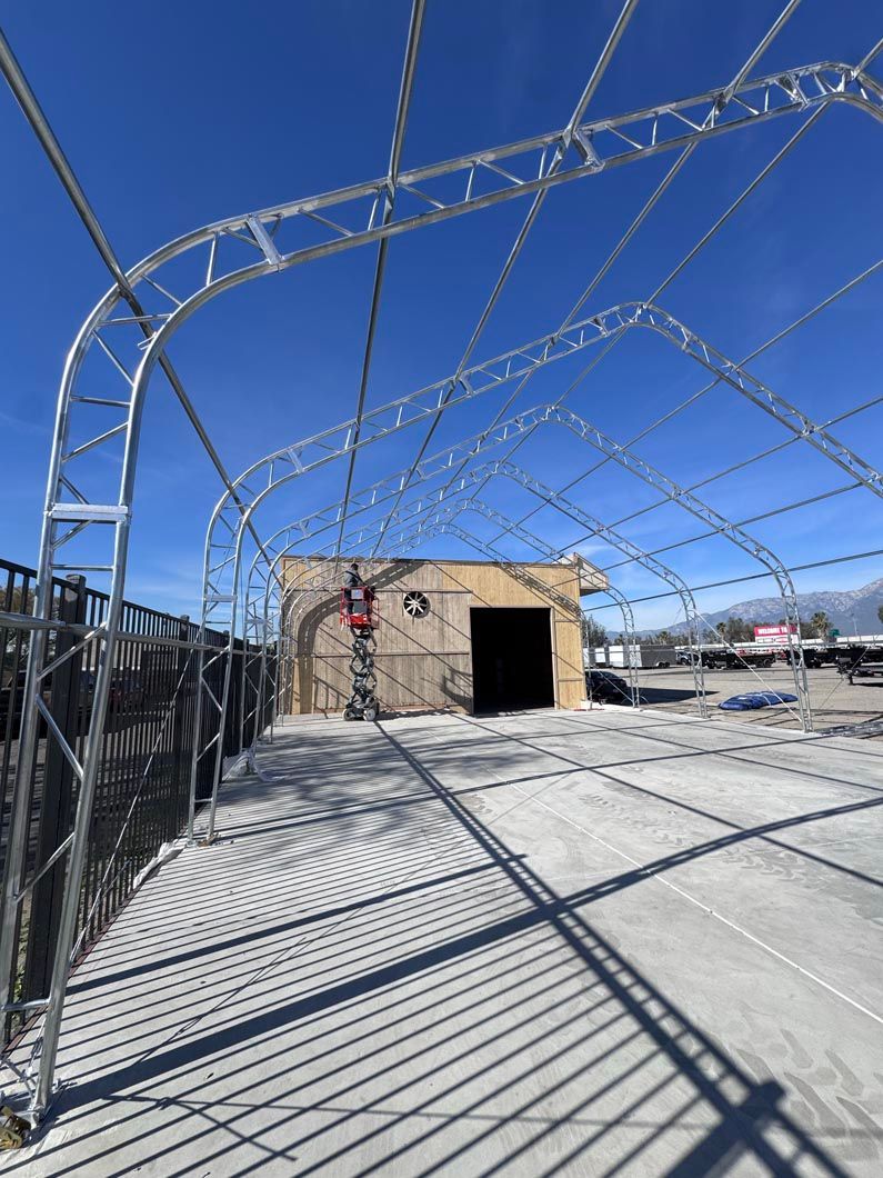 Chain-link fenced outdoor yard with barbed-wire archway, concrete ground, and a small stone building under a blue sky