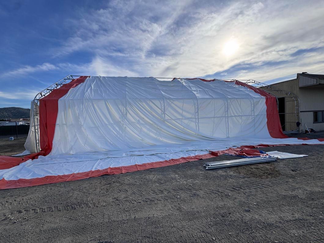 Large white-and-red tarp-covered structure on a gravel lot under a cloudy sky