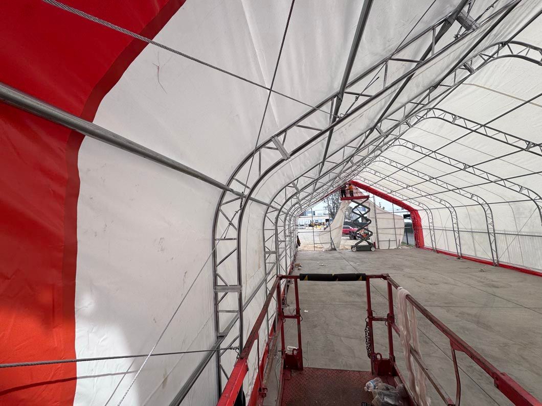 Tunnel-like covered walkway with red and white fabric walls and metal framing, leading to an open street.