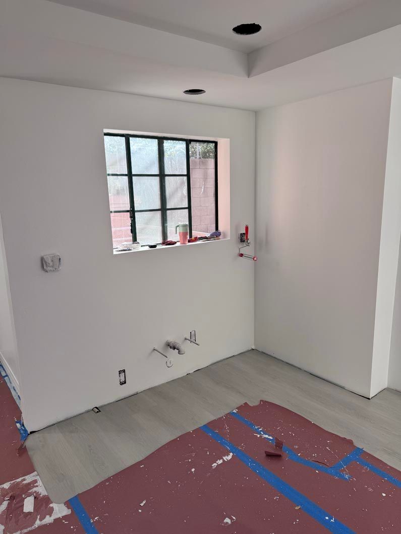 Empty white room with a small window, gray floor, and red protective covering on the floor.