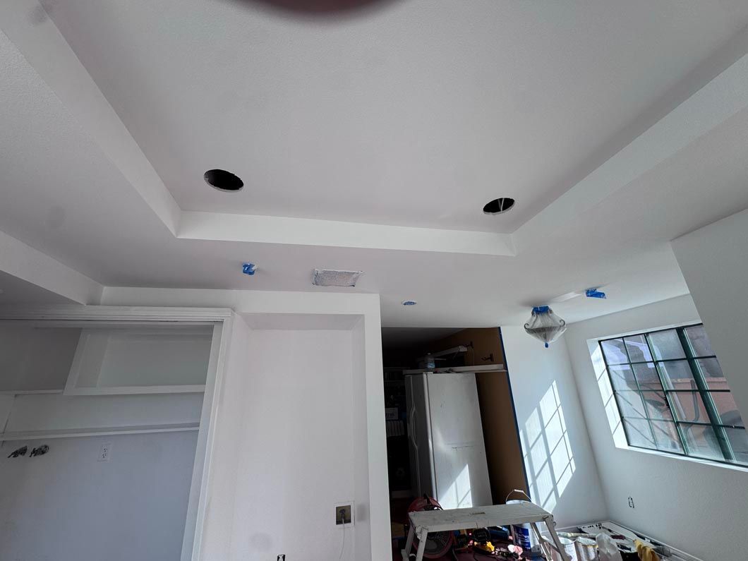 Empty white room under renovation with recessed ceiling lights, open closet, and sunlight from a window.