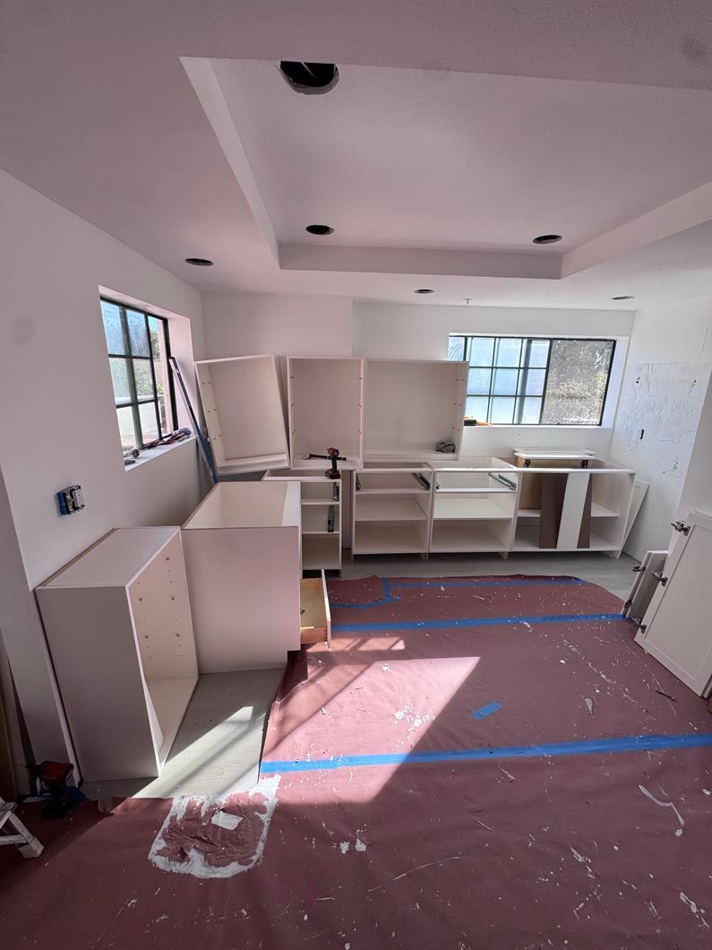 Empty room with white cabinets, windows, and pink protective floor covering during renovation