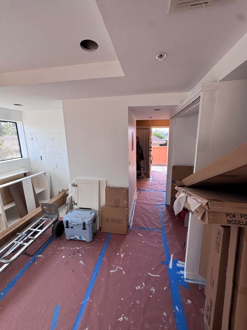 Renovated hallway with covered floor, tools, and boxes; doorway opens to bright exterior.
