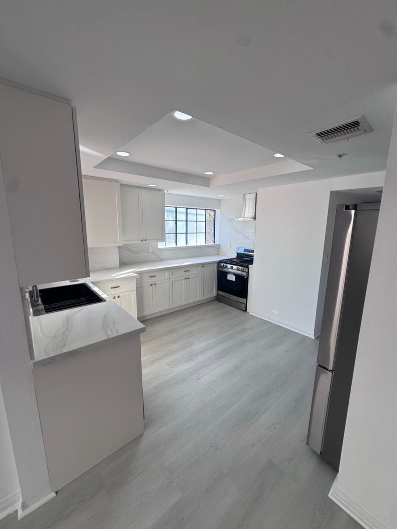 Bright white modern kitchen with cabinets, stove, window, and light wood flooring