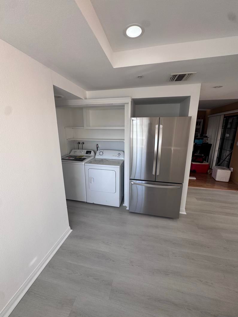 Small kitchen nook with stainless fridge, sink, cabinets, and gray flooring in a bright apartment
