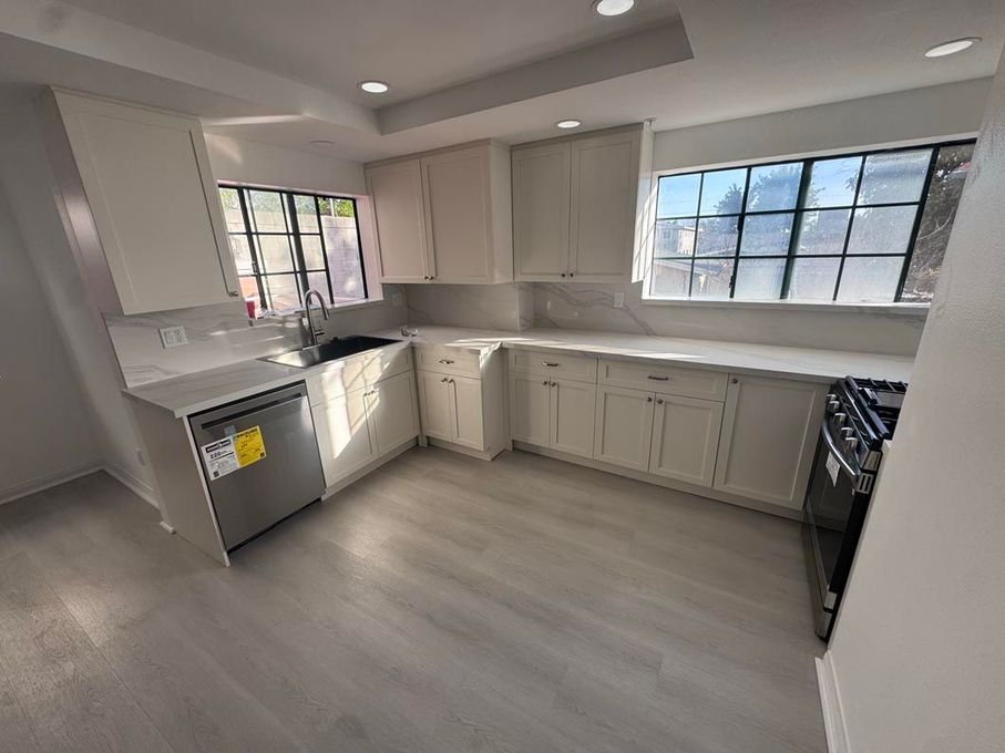 Empty modern kitchen with white cabinets, gray floor, and large windows letting in daylight