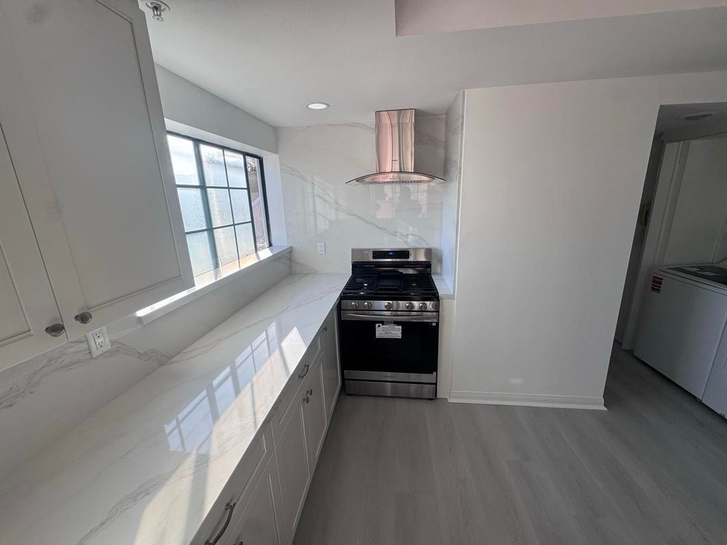 Bright white galley kitchen with window, black stove, and light gray flooring