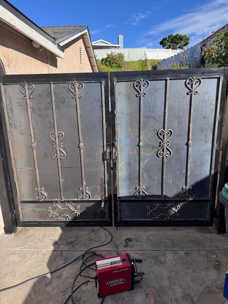 Closed gray metal gate with decorative scrollwork and a red power unit on the driveway in front of it