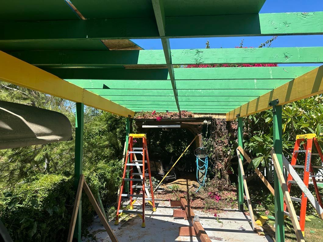 Two ladders under a green and yellow pergola frame, with workers at the far end of a garden path.