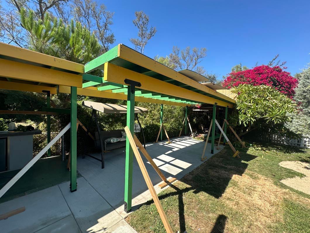 Colorful patio pergola with slanted roof, green posts, and lounge chairs in a sunny backyard