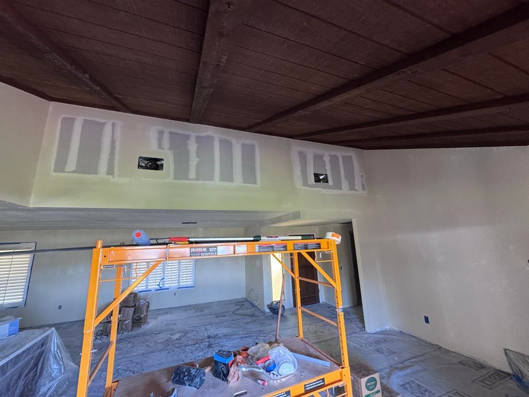 Interior room under renovation with drywall, exposed ceiling, and orange scaffolding in the center.