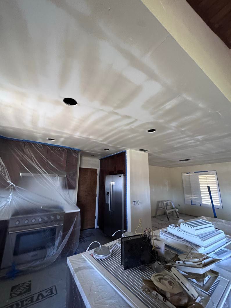 Partially renovated kitchen with stacked materials, covered cabinets, and plastic sheeting on appliances