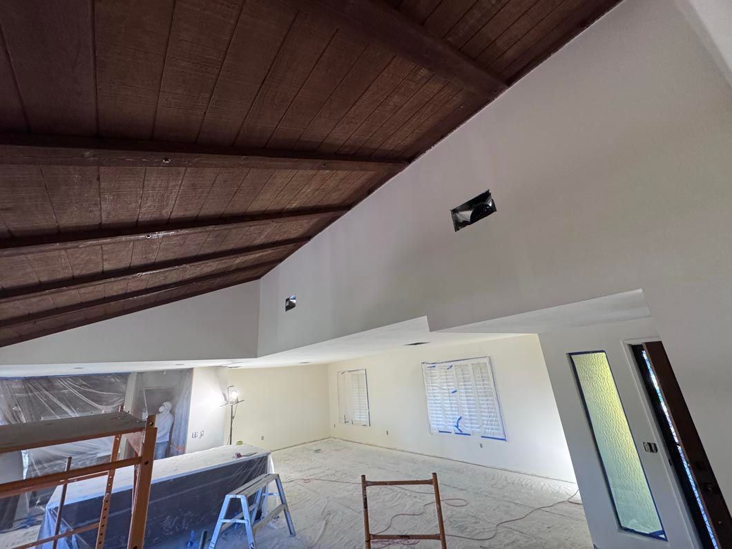 Interior room with wood ceiling, white walls, blue tarp-covered area, and a ladder under renovation